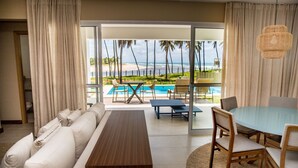 A hotel room with a sofa, a dining table, and chairs. There is a view of a pool and palm trees outside. - Baixio Residences by ¼ UmQuarto. (Baixio)