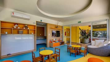 Uma área de recreação infantil com mobiliário colorido, um quadro branco e uma planta grande.