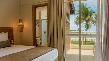 Quarto de hotel com cama, chuveiro e varanda com vista para palmeiras.