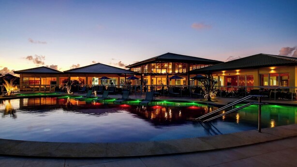 Un hôtel doté d’une piscine, d’un espace extérieur aménagé et d’un bâtiment bien éclairé au crépuscule.