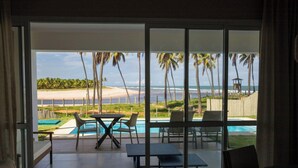 Un salon moderne doté d’une grande porte-fenêtre coulissante donnant sur un espace piscine avec vue sur la plage et les palmiers.