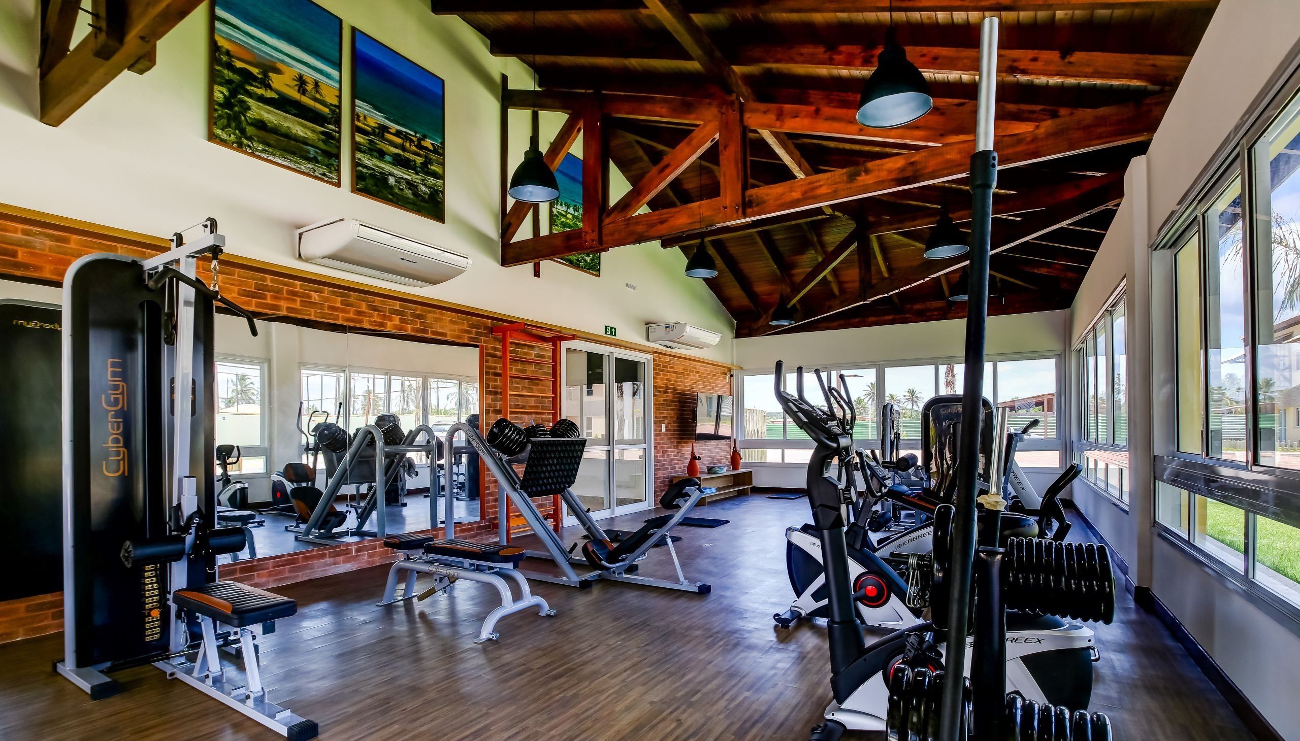 Un gimnasio con equipo de ejercicio diverso, ventanas amplias y un techo alto con vigas a la vista.