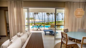 Habitación de hotel con sofá, mesa de comedor y vistas a la playa y al océano.