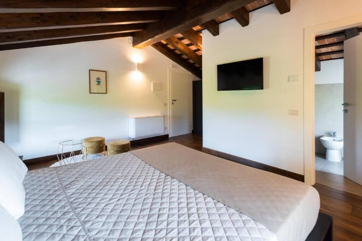 A bedroom with a large bed, a television mounted on the wall, and a wooden ceiling.