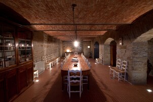 Una habitación larga y estrecha con una mesa y sillas de madera, paredes de piedra y techo de ladrillo.