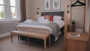 A neatly arranged bedroom with a bed, a bench, a bedside table, a hanging light, and a window.