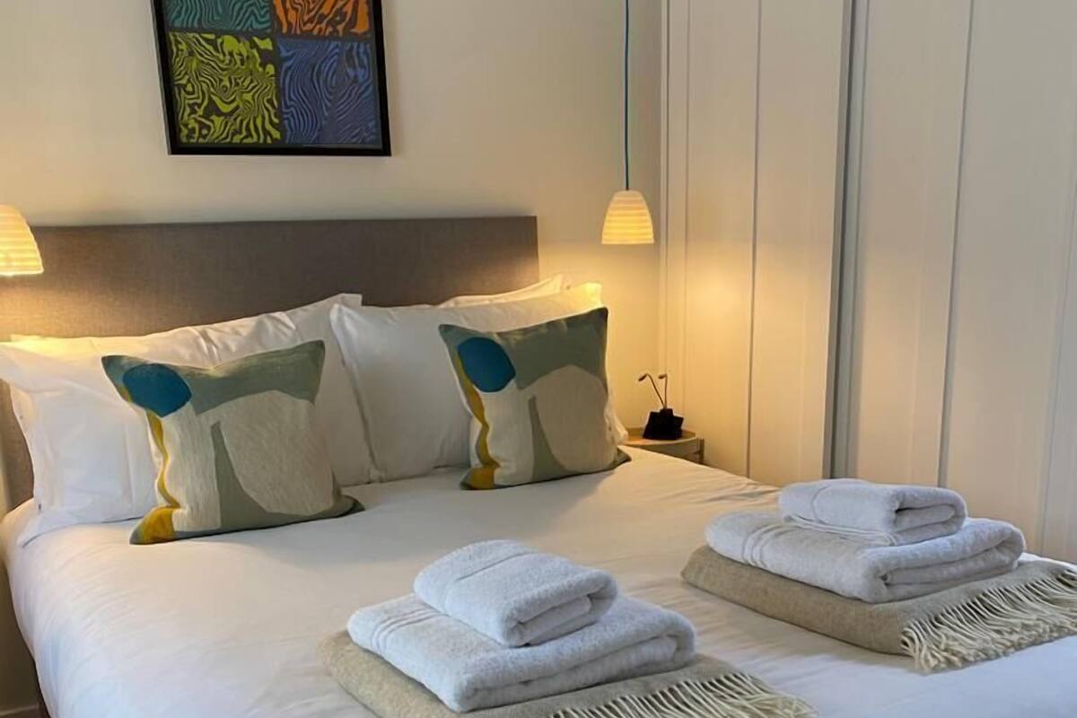 A neatly made bed with white linens, two folded towels, and a decorative pillow.