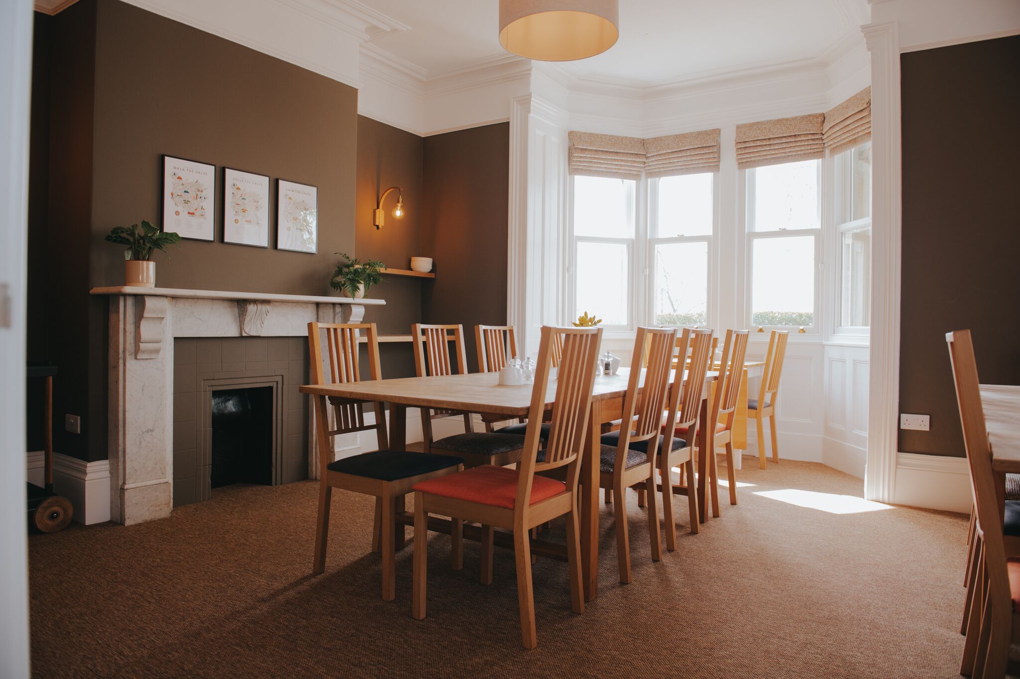 A dining area with a fireplace, wooden chairs, and a large window with curtains.