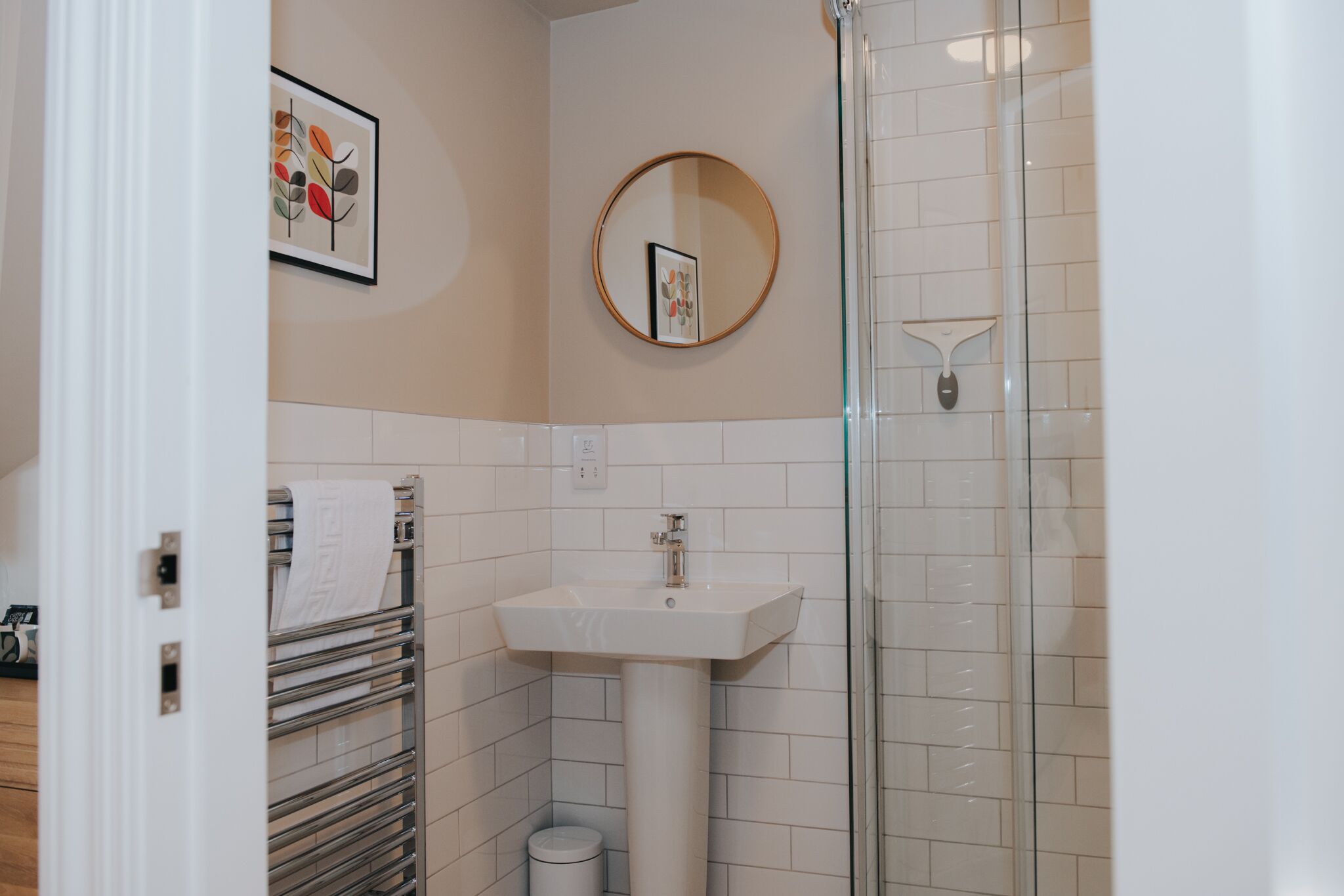 Un baño con lavamanos blanco, cabina de ducha de vidrio, perchero y un cuadro en la pared.