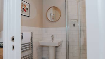 Un baño con lavamanos blanco, cabina de ducha de vidrio, perchero y un cuadro en la pared.