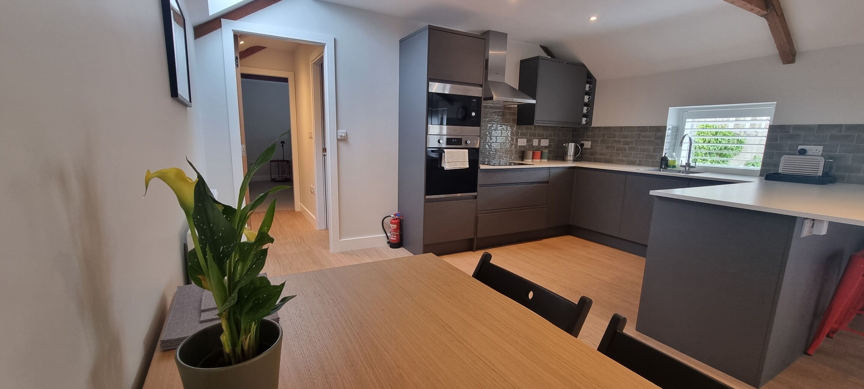 A modern kitchen with grey cabinets, a stainless steel oven, and a window with a view of greenery.