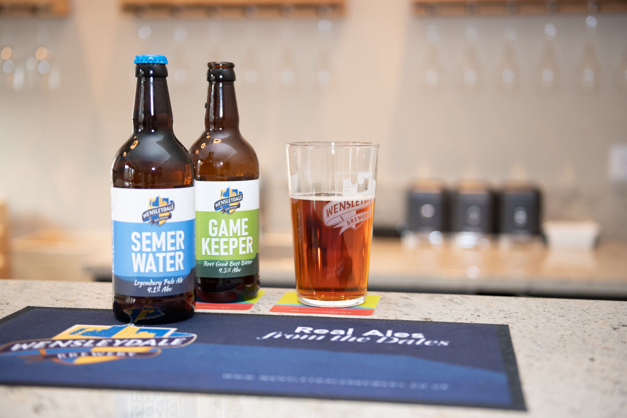 Two bottles of beer and a glass on a counter.