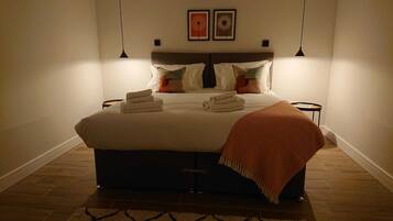 Een net opgemaakt bed met kussens en dekbed, een klein nachtkastje en twee wandlampen.
