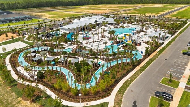 An aerial view of a resort with multiple swimming pools, palm trees, and a parking area. - EV_15883 - 6BR / 5BA Luxury Villa w/ Private Pool, Theater, Themed Kids' Room (Clermont)