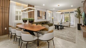 A modern living room with a wooden dining table, white chairs, a sofa, and a TV. - EV_15883 - 6BR / 5BA Luxury Villa w/ Private Pool, Theater, Themed Kids' Room (Clermont)