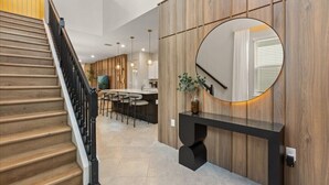 A modern interior with a wooden staircase, a round mirror, and a bar area with stools. - EV_15883 - 6BR / 5BA Luxury Villa w/ Private Pool, Theater, Themed Kids' Room (Clermont)