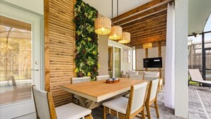 An outdoor dining area with a wooden table and chairs, a vertical garden wall, and wicker pendant lights. - EV_15883 - 6BR / 5BA Luxury Villa w/ Private Pool, Theater, Themed Kids' Room (Clermont)