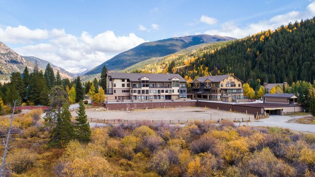 A multi-story hotel with a large parking area, surrounded by autumn foliage and mountains.