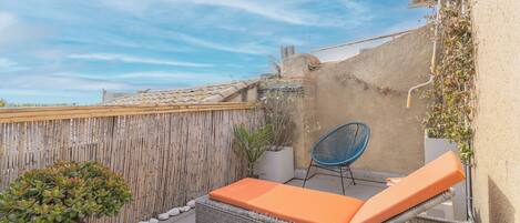 A rooftop terrace with a wicker lounge chair, a small potted plant, and a bamboo fence.
