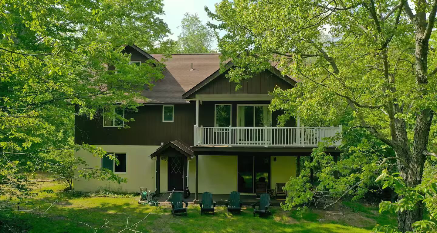 A two-story house with a balcony, surrounded by lush greenery.