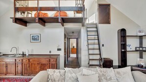 Spazio abitativo in stile loft con cucina, una scala e un angolo relax con cuscini decorati.