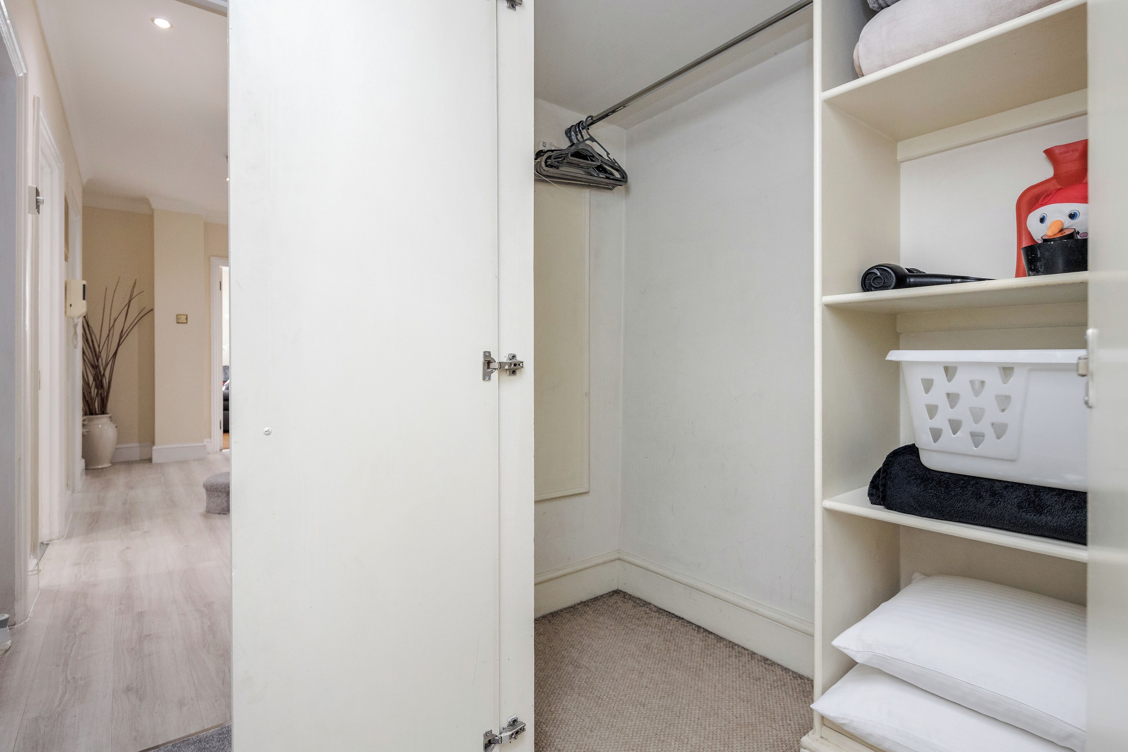 A walk-in closet with a hanging rack, shelves with folded towels, and a door leading to another room.