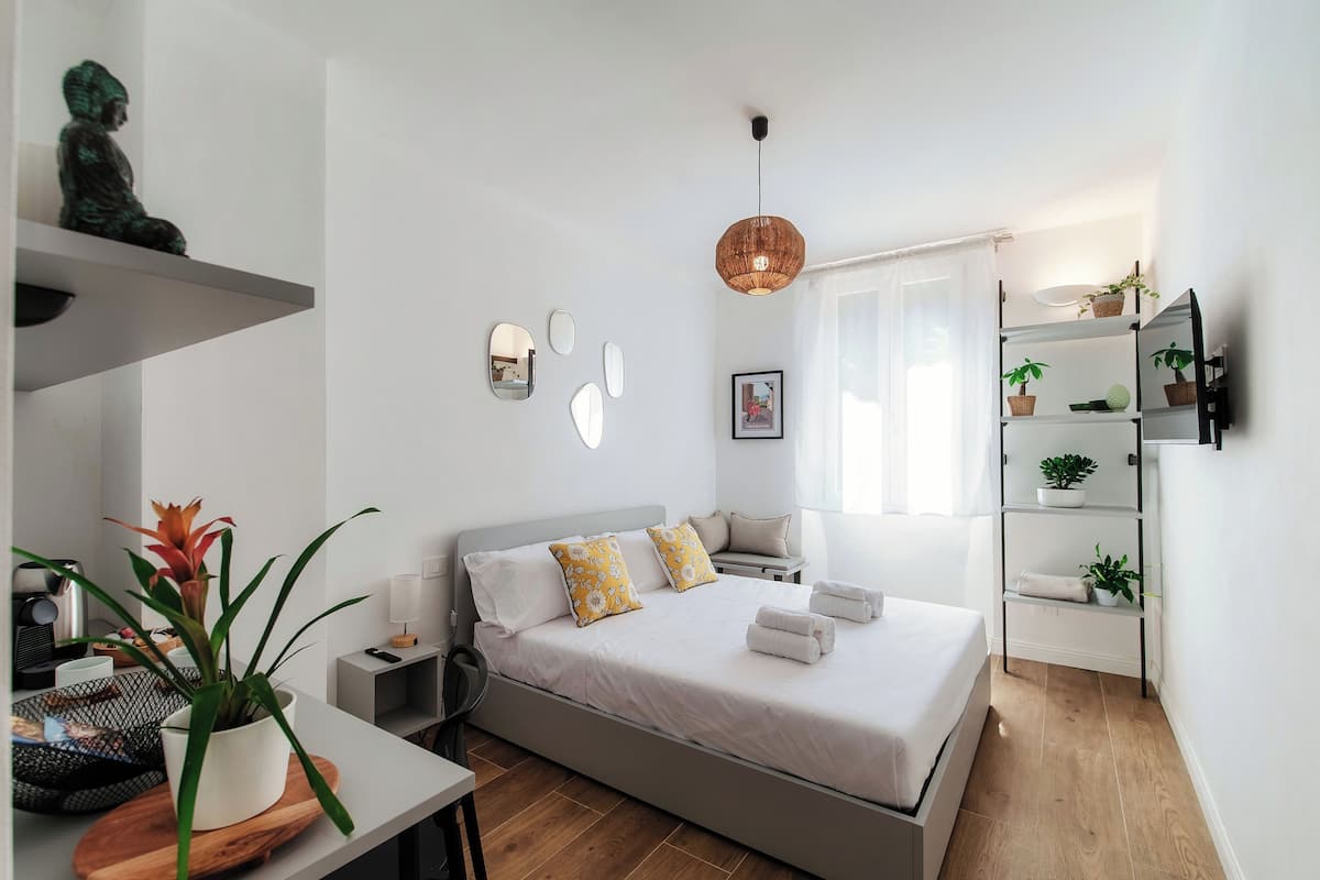 A modern bedroom with a bed, bedside tables, a desk, and a shelving unit.