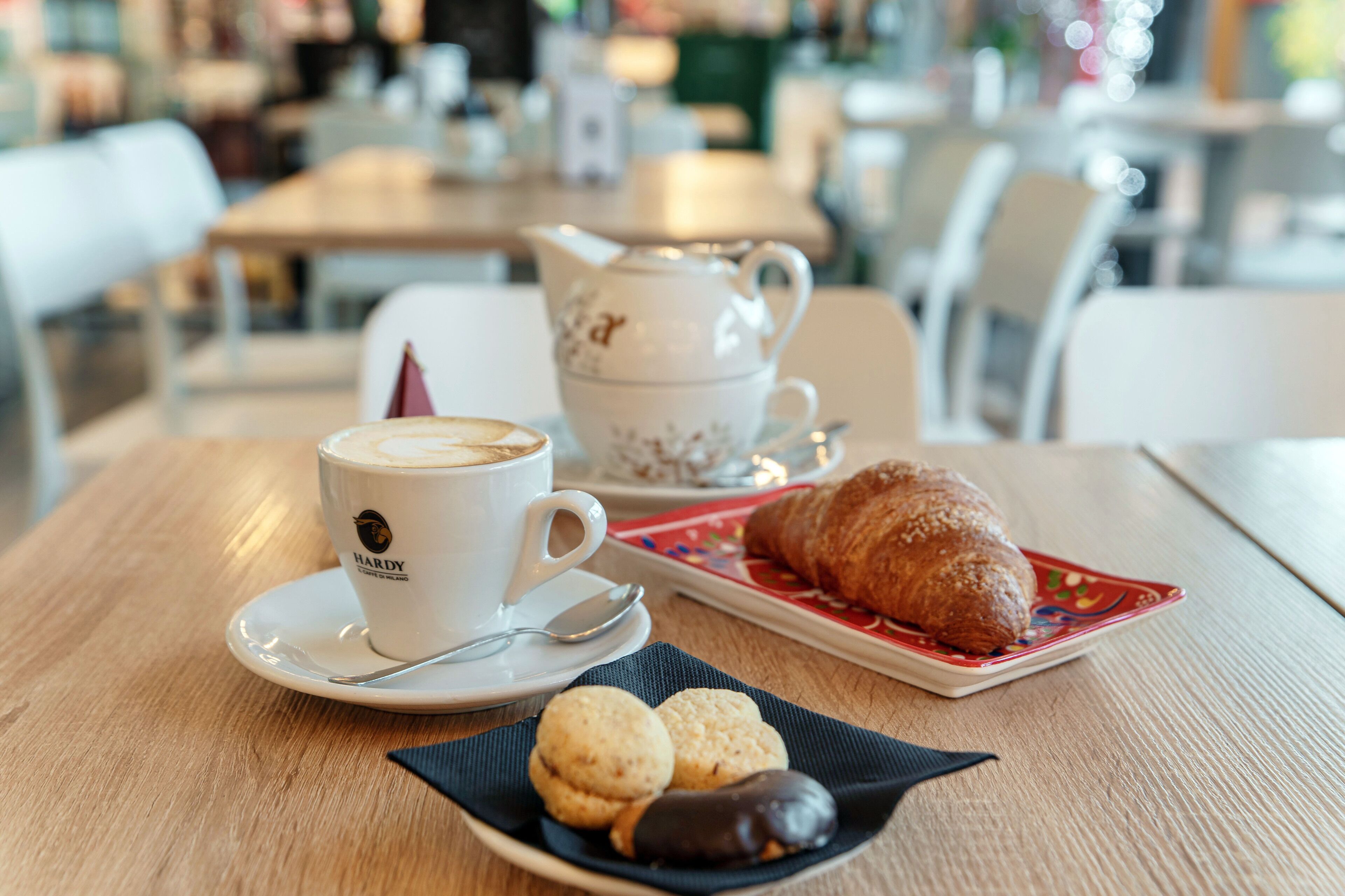 Una mesa con una taza de café, una tetera, un croissant y galletas.