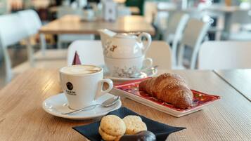 Una mesa con una taza de café, una tetera, un croissant y galletas.
