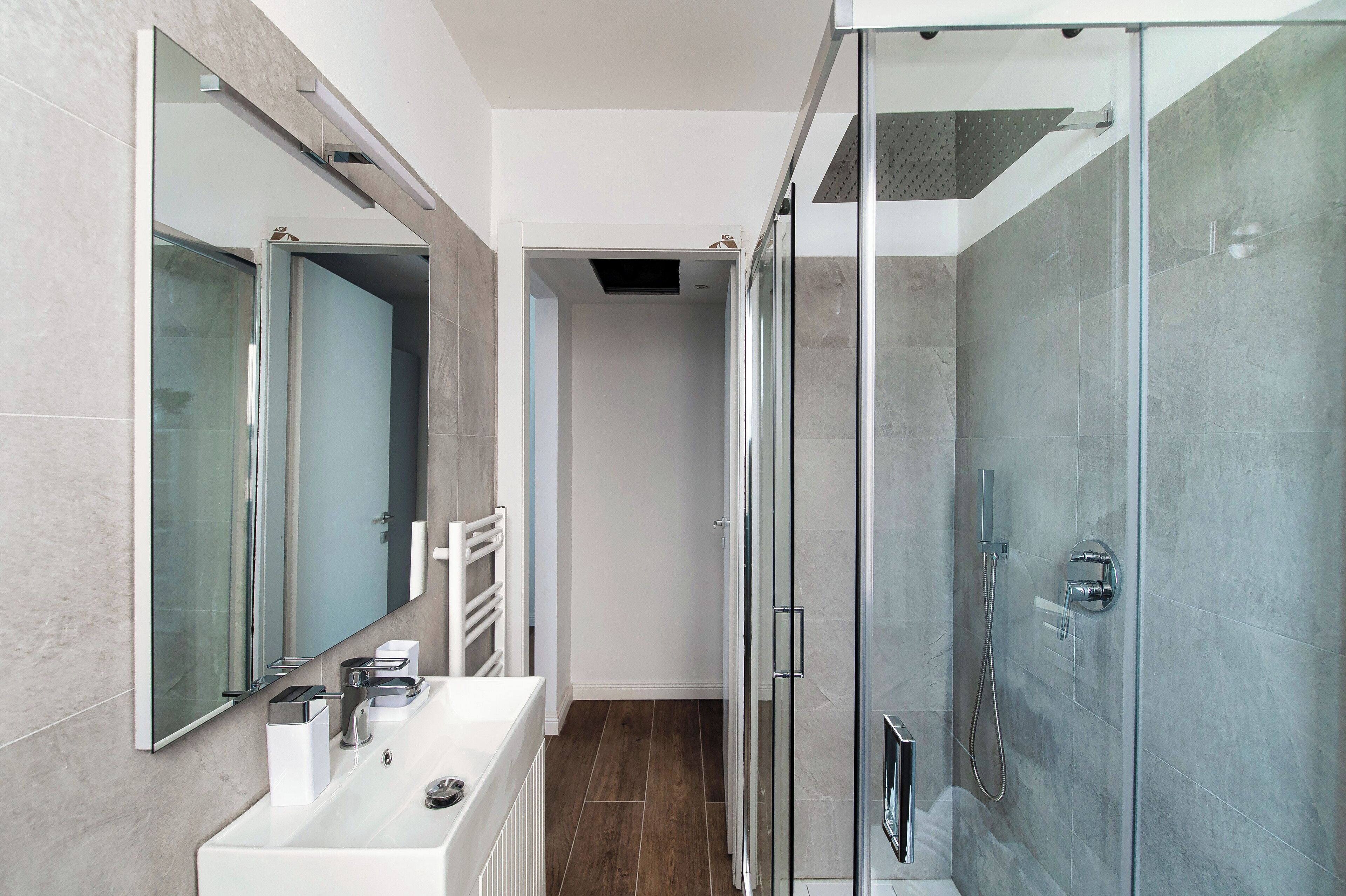 Un baño moderno con ducha envuelta en vidrio, un lavabo blanco y un espejo grande.