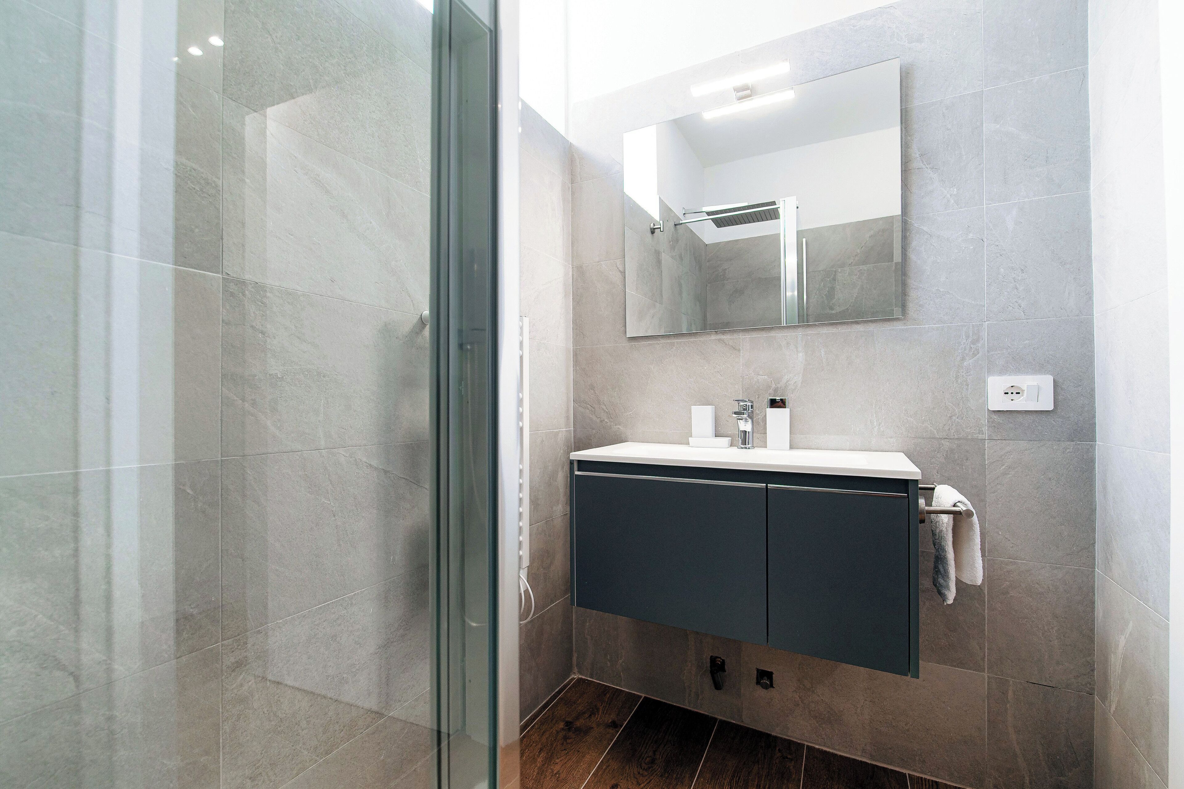 A modern bathroom with a glass shower enclosure, a vanity with a mirror, and a towel rack.