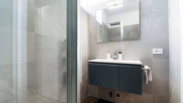 A modern bathroom with a glass shower enclosure, a vanity with a mirror, and a towel rack.
