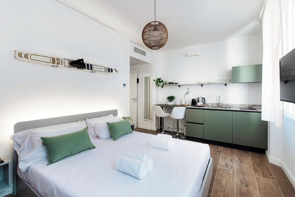 A modern hotel room with a neatly made bed, a small kitchenette, and a dining area.