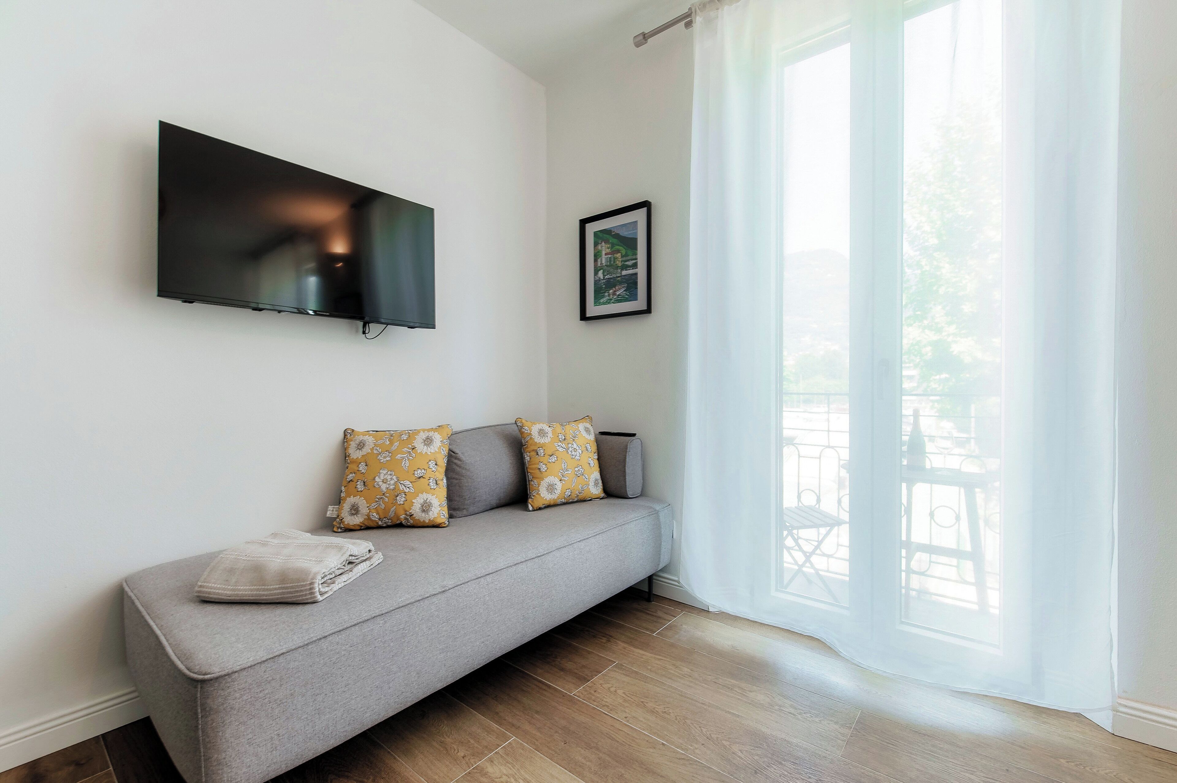 Una sala de estar moderna con un sofá gris, un televisor de pantalla plana montado en la pared y un cuadro enmarcado encima.