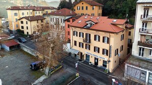 A multi-story building with a pizzeria on the ground floor, surrounded by other buildings and a hilly landscape. - Casa Batèl Suites & Apartments (Como)