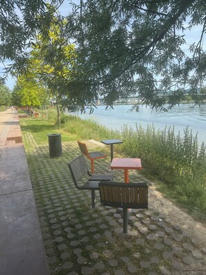 Een park aan de rivier met een verharde looppad, banken en tafels.