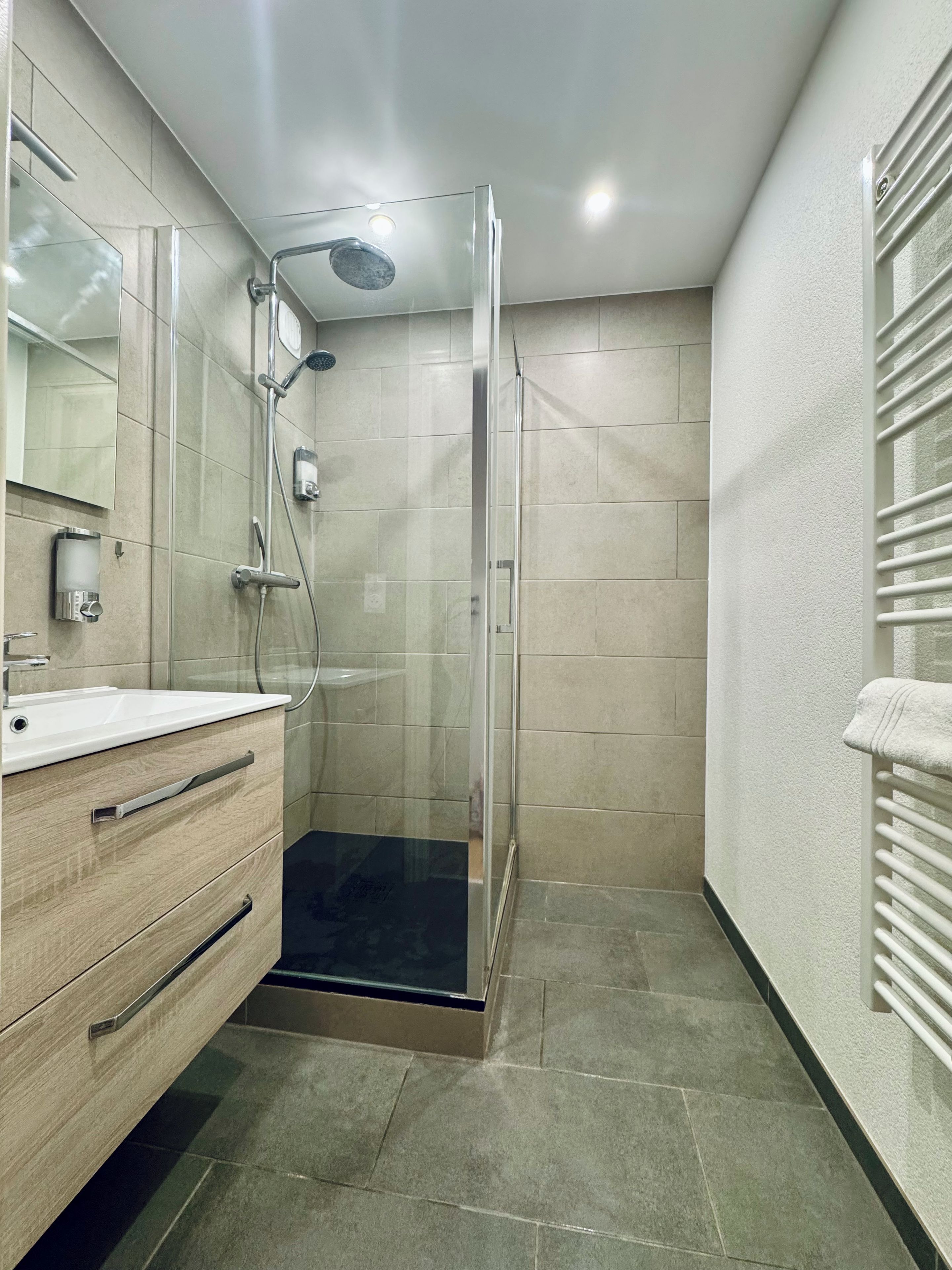 Ein modernes Badezimmer mit einer gläsernen Dusche, einem Holzbadezimmerwaschbecken mit weißem Waschbecken und einem Handtuchhalter an der Wand.