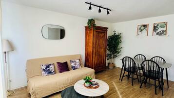 Una sala de estar con un sofá, una mesa redonda, un aparador de madera, un espejo y un comedor con sillas y una mesa.