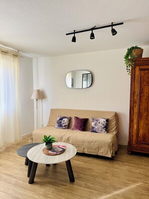 Een woonkamer met een bank, een ronde salontafel met een plant, een spiegel en een lamp.