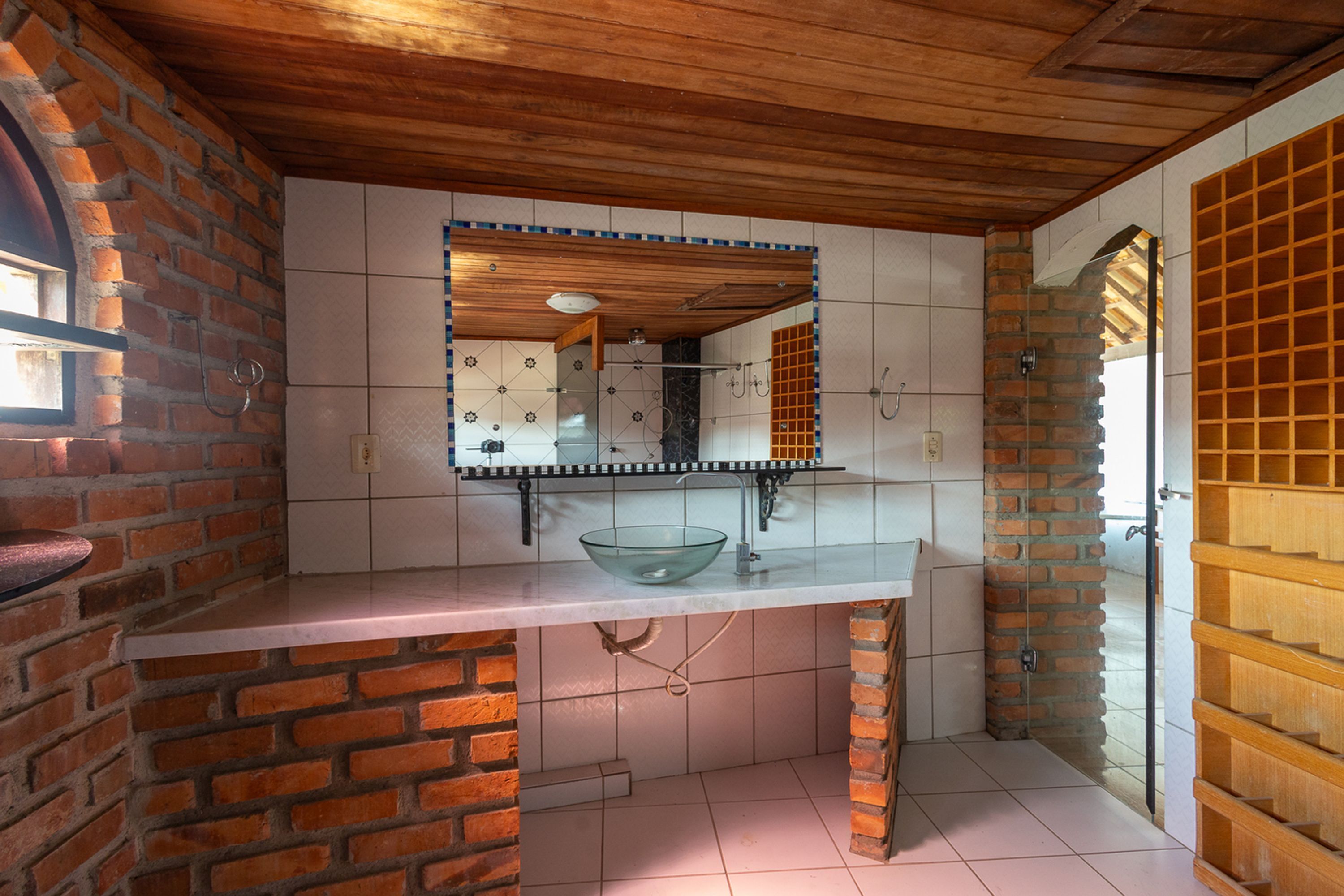 A bathroom with a glass sink, white tiles, and a wooden ceiling.