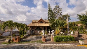 Un edificio pequeño con techo de tejas y fachada de ladrillo, rodeado de plantas en macetas y una estatua.