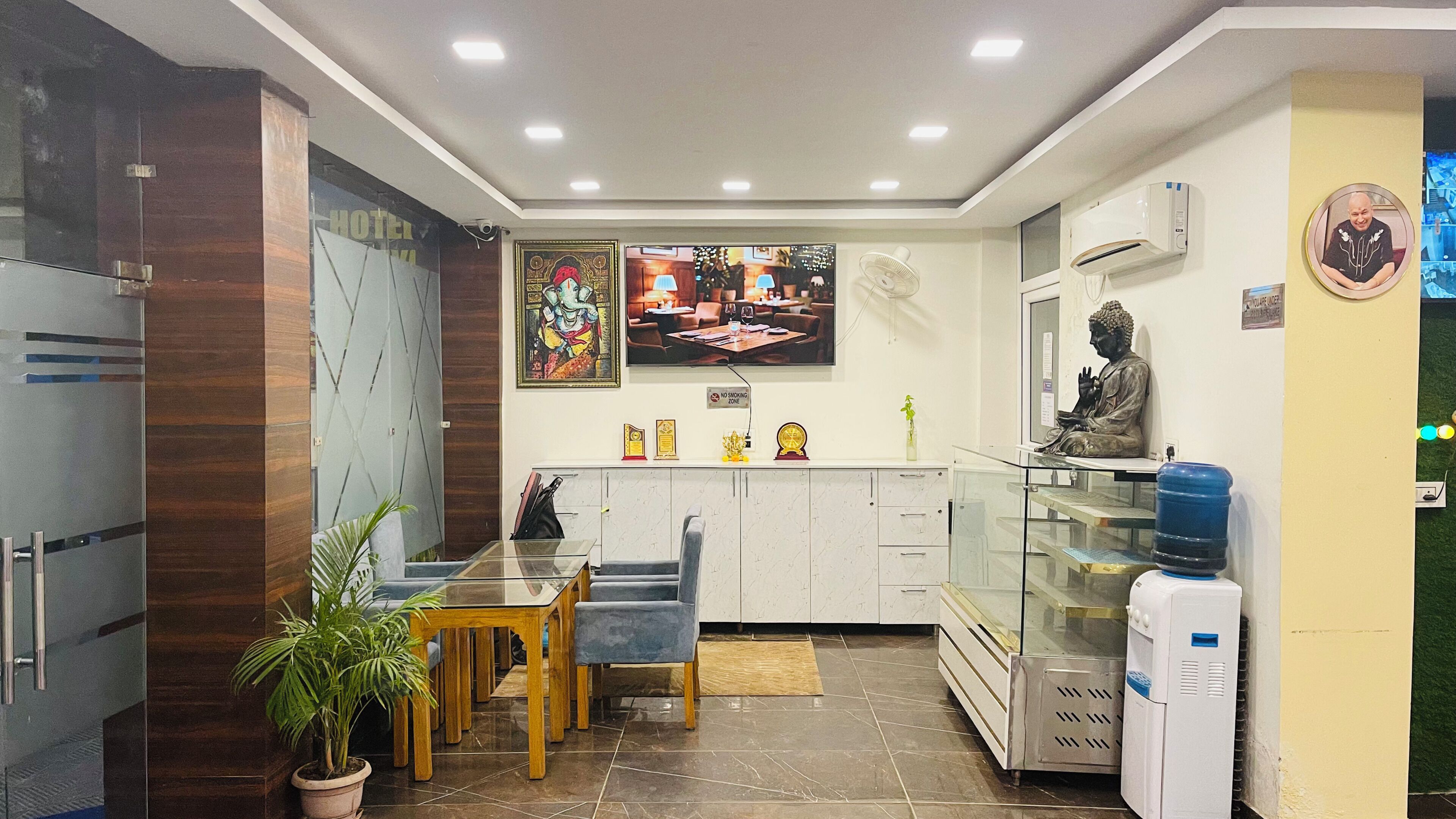 A hotel reception area with a glass partition, a Buddha statue, a water dispenser, and a 'No Smoking' sign.