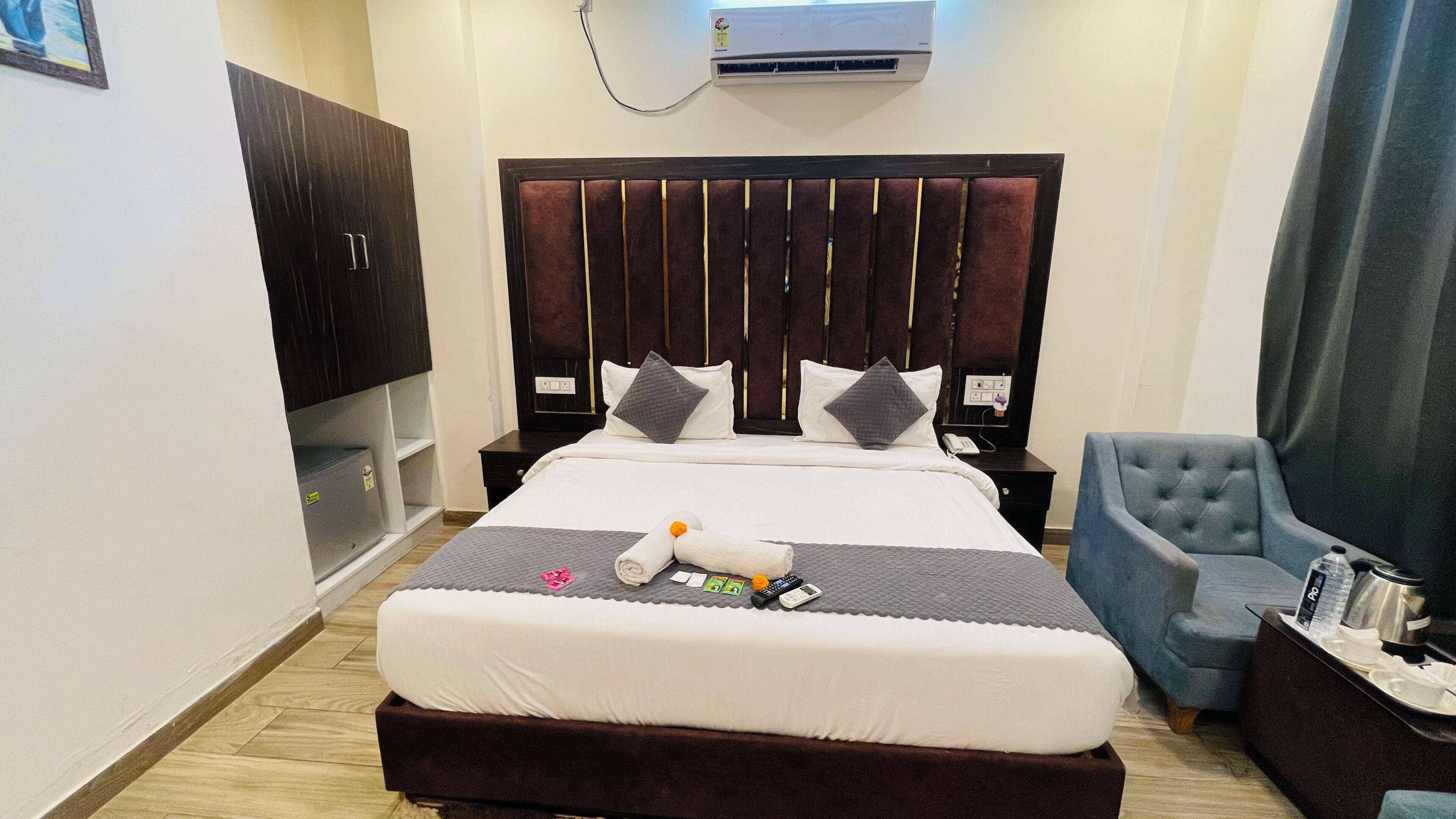 A hotel room with a large bed, a bedside table, a chair, and an air conditioning unit.