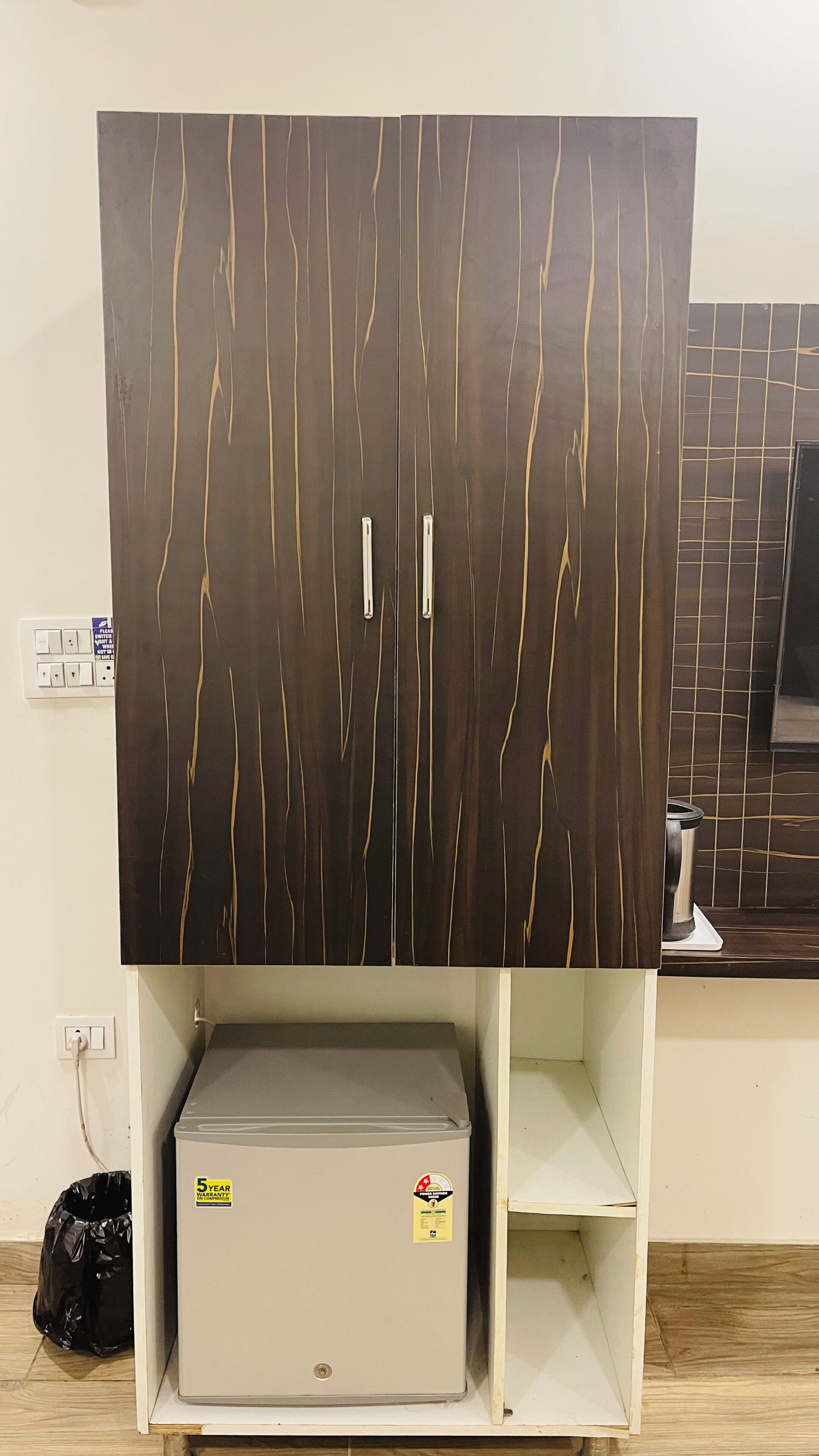 Un armario con detalles en madera oscura y líneas verticales, un electrodoméstico pequeño debajo y un reverso con azulejos.