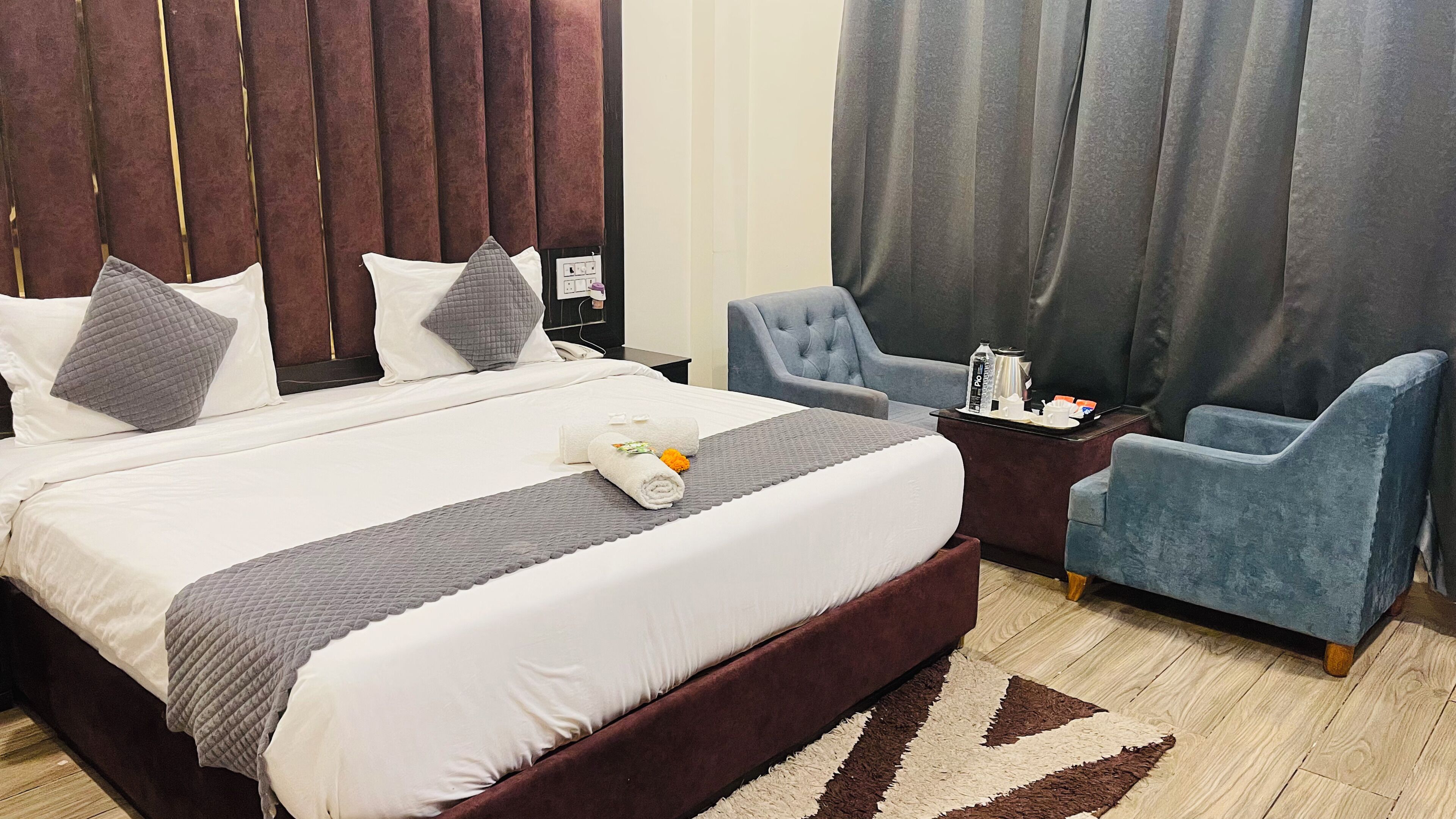 Hotellihuone, jossa on suuri sänky, kaksi nojatuolia, pieni sivupöytä, jossa on kahvinkeitin, ja näkymä kaupunkiin.