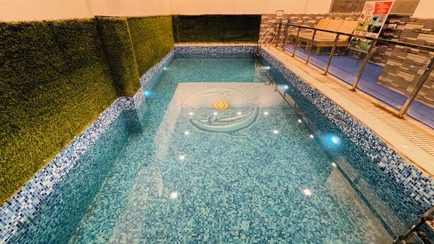 Ein Schwimmbecken mit Mosaikfliesen, einer grünen Rasenumrandung aus Kunstgrün und einem Sonnendesign auf dem Boden.