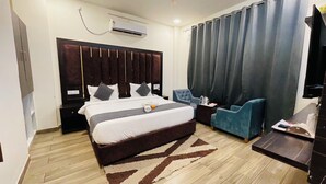 Ein Hotelzimmer mit einem großen Bett, einem Schreibtisch, einem Sessel, einem Fernseher und einer Klimaanlage.