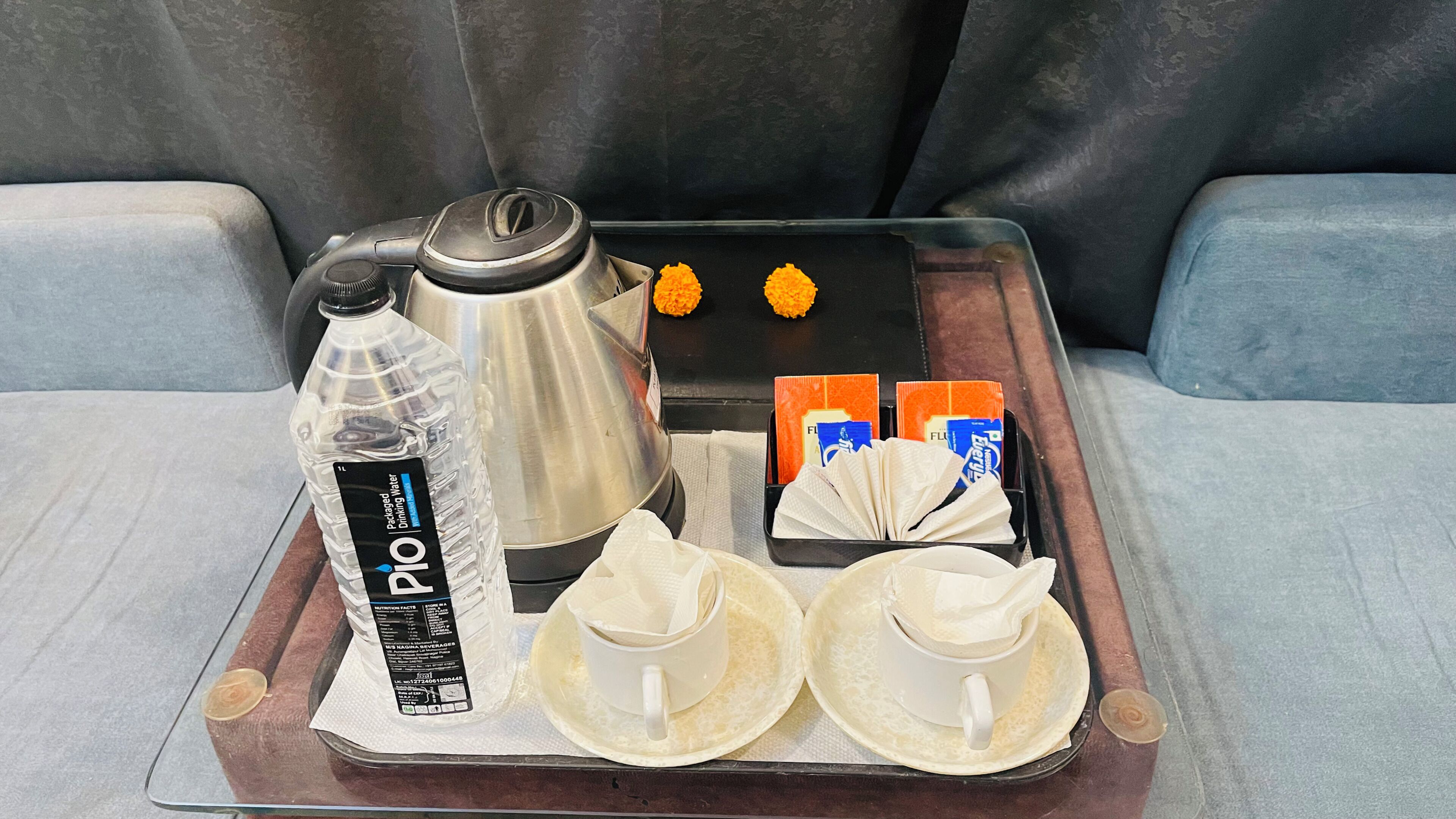 A tray with a water bottle, a coffee pot, a box of tissues, and two cups with napkins.