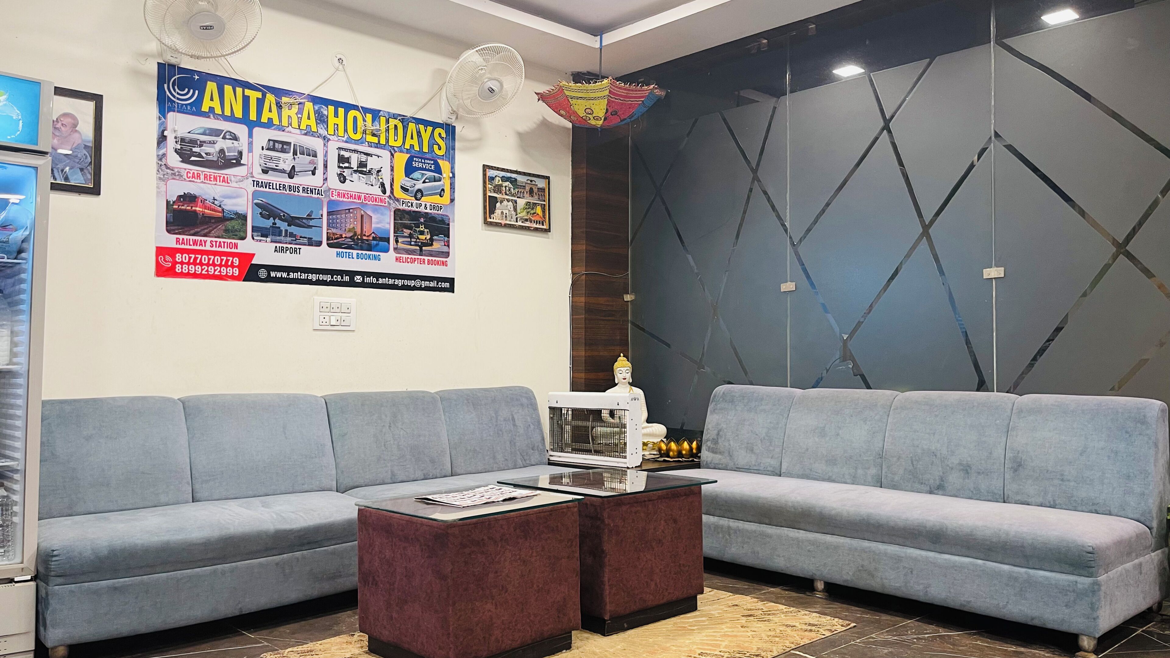 Un espace d’accueil comprenant deux canapés gris, une table basse, une statue de Bouddha et un mur orné d’un motif géométrique.