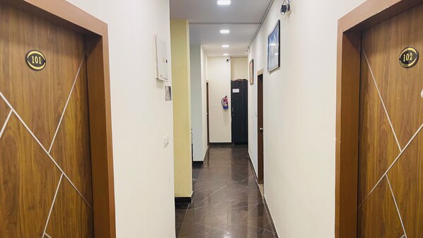 A hallway with wooden doors marked 101 and 102, a fire extinguisher, and a ceiling-mounted light fixture. - Hotel Shreya Galaxy (Haridwar)